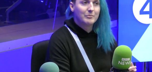 Laura Kate Dales wears a dark top and has blue long hair with an undercut while appearing during a BBC Radio interview discussing Gender Recognition Certificates