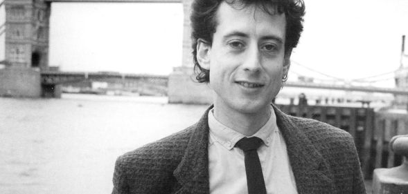 Peter Tatchell in a photograph promoting his candidacy in the 1983 Bermondsey by-election. He is pictured by a bridge wearing a suit in a black and white shot.