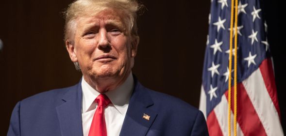 Donald Trump smirking in front of a US flag