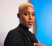 A promo shot of actor Jerrie Johnson wearing a black dress with short white-blonde hair standing in front of a blue and white background