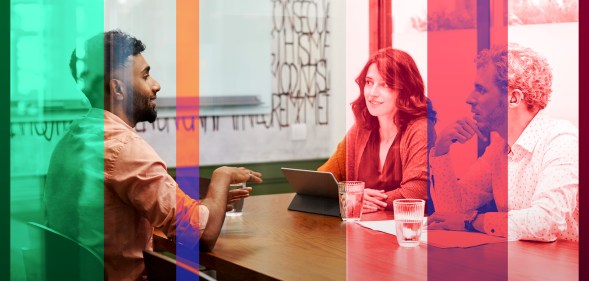 A man in a beard is sitting across from a man and woman in a conference room setting in an office.