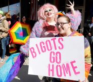 A person holds up a sign reading "Bigots go home" as a drag queen poses in the background at a protest in support of Drag Story Hour