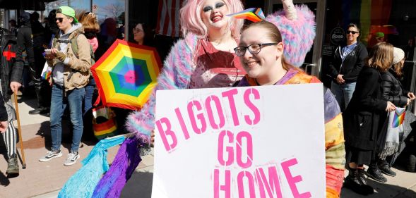 A person holds up a sign reading "Bigots go home" as a drag queen poses in the background at a protest in support of Drag Story Hour