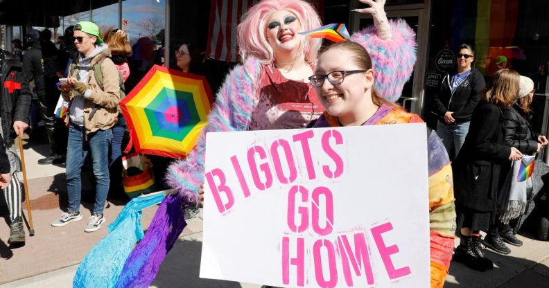 A person holds up a sign reading "Bigots go home" as a drag queen poses in the background at a protest in support of Drag Story Hour