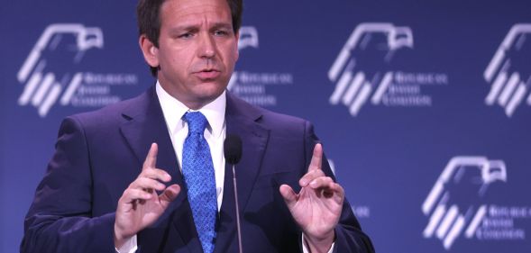 Florida governor Ron DeSantis wears a suit and tie as he gestures with one finger raised upwards on both hands during a speech