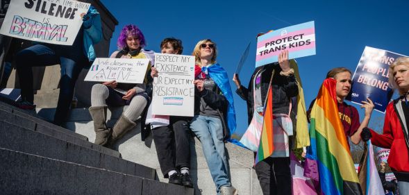 A crowd of people hold up LGBTQ+ and trans Pride flags as well as signs in support of the community as they sit on the Kentucky state capitol steps to protest against the passing of SB 150