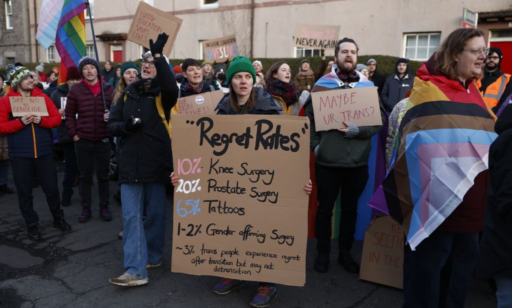 A person holds up a sign during a trans protest that lists the percentage of people who regret certain surgeries. According to the science used in the study, very few trans people regret gender-affirming surgery