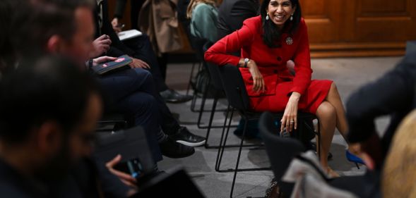 Suella Braverman sitting in a chair, laughing with people surrounding her