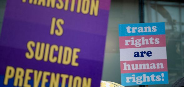 A person holds up a sign reading 'Transition is suicide prevention' while another holds up a sign reading 'trans rights are human rights' during a protest