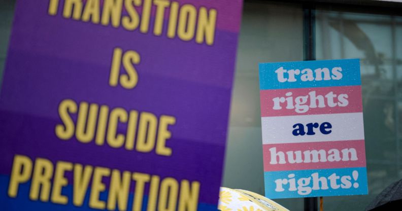 A person holds up a sign reading 'Transition is suicide prevention' while another holds up a sign reading 'trans rights are human rights' during a protest