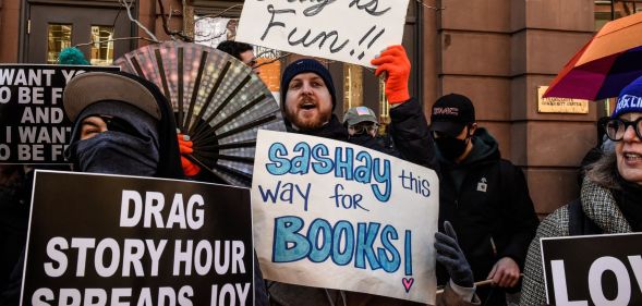 A person in a pro-drag rally holding signs reading 'drag story hour spreads joy'