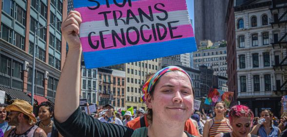 Trans protestor holding up a sign that reads "stop trans genocide"