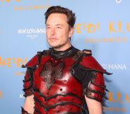 Twitter boss Elon Musk wears a red and black armour like outfit as he stands in front of a light blue and yellow background