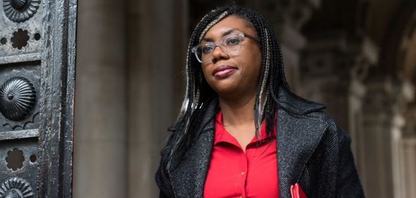 Kemi Badenoch wearing a black blazer and red blouse walking outdoors.