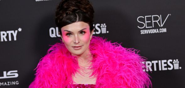 Dylan Mulvaney wears pink feather boa and pink eyeshadow against a black background