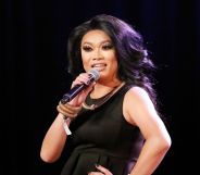 RuPaul's Drag Race queen Jujubee wears a dark wig and dress while smiling and speaking into a microphone.