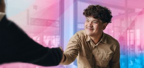 In this image, a trans person is wearing a khaki coloured shirt and is shaking hands with someone.