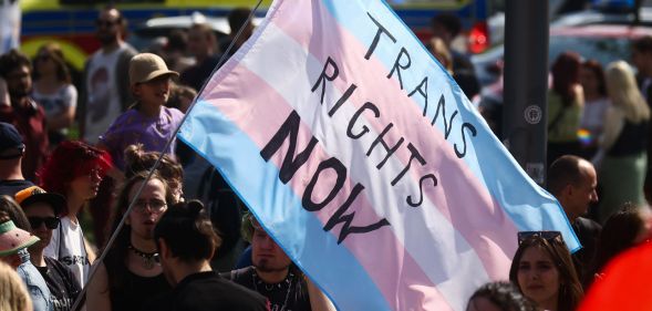 A person holds a giant trans flag that reads 'trans rights now'