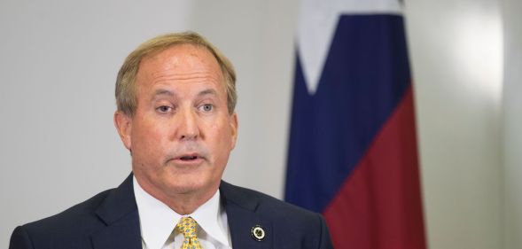 Texas attorney general Ken Paxton, who has repeatedly pushed back on trans rights in the states, speaks to people off camera while wearing a white shirt, yellow tie and dark suit jacket