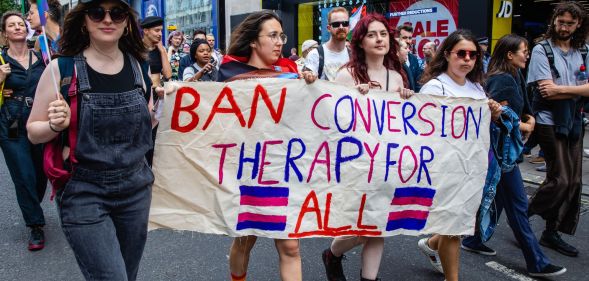 Activists hold a sign reading "ban conversion therapy for all."