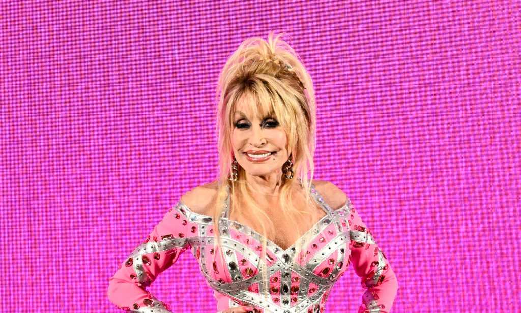 Dolly Parton in a pink patterned dress against a pink background