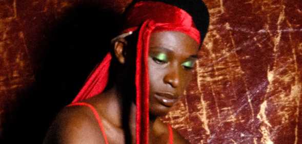 A character from Soft Bwoi - a Black man wearing a red durag and green eye shadow