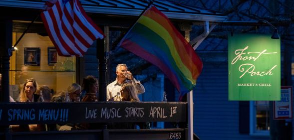 Residents drink on the balcony of a restaurant as the sun goes down, while a Pride and US flag wave.