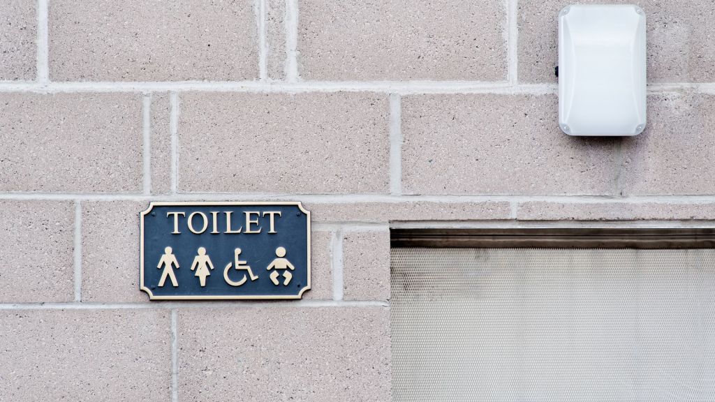 Stock photo shows a sign for gender-neutral toilets, featuring symbols for men, women, disabled people, and baby changing