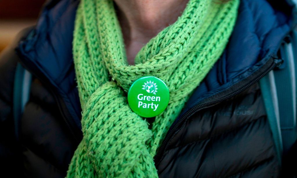 A Green Party member wearing a scarf and a Green Party badge.