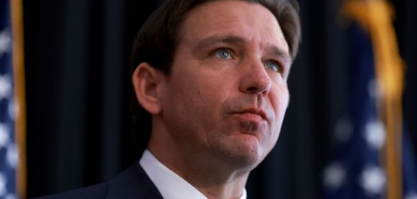 Ron DeSantis looking upwards while American flags stand beside him.