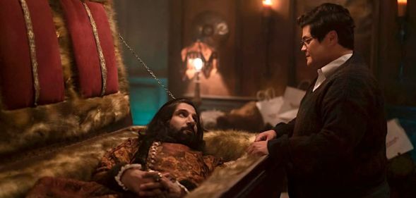 A still from What We Do in the Shadows with vampire character Nandor in a coffin with human familiar Guillermo talking to him