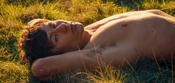 Barry Keoghan as Oliver in Saltburn, he's topless lying in the grass