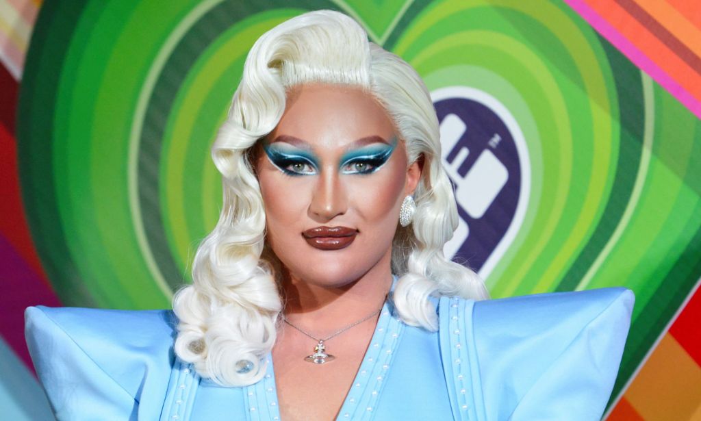 Drag Race Uk star The Vivienne, who is wearing a blonde wig and blue outfit, stares at the camera