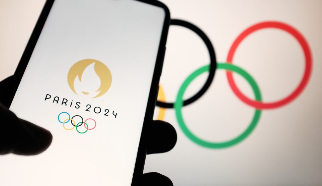 In this photo illustration a 2024 Summer Olympics (Paris 2024 Olympic Games) logo is seen on a smartphone and Olympic rings on a computer screen in Athens, Greece on April 19, 2023. (Photo illustration by Nikolas Kokovlis/NurPhoto via Getty Images)