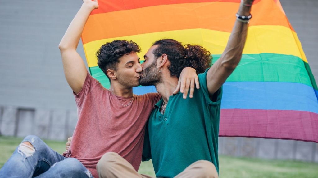 Stock image of two men kissing beneath a Pride flag