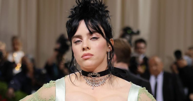 Billie Eilish with black hair done up in a bun, wearing a black choken and a strappy green dress at the 2022 MET Gala.