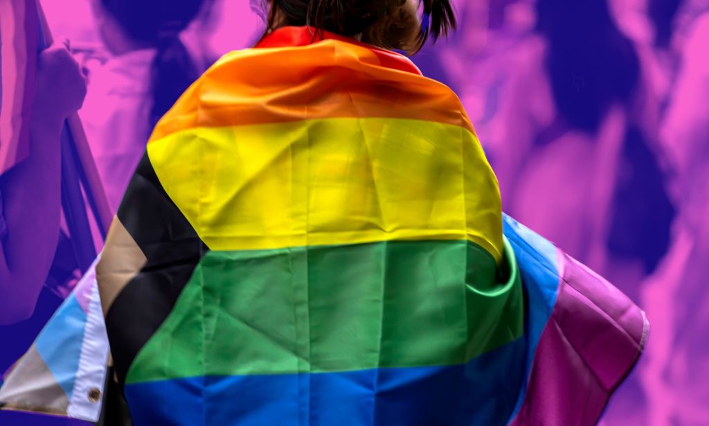 This is an image of the back of a person draped in the intersectional Pride flag.