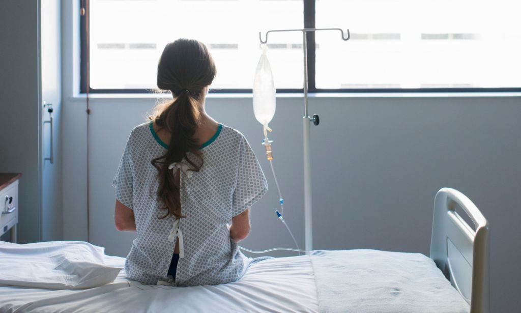 A person sits on a hospital bed looking out a window.