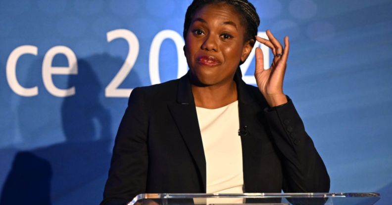 This is an image of UK government minister Kemi Badenoch. She is speaking at an event. She is wearing a black blazer and white top and has a look of confusion in her face.