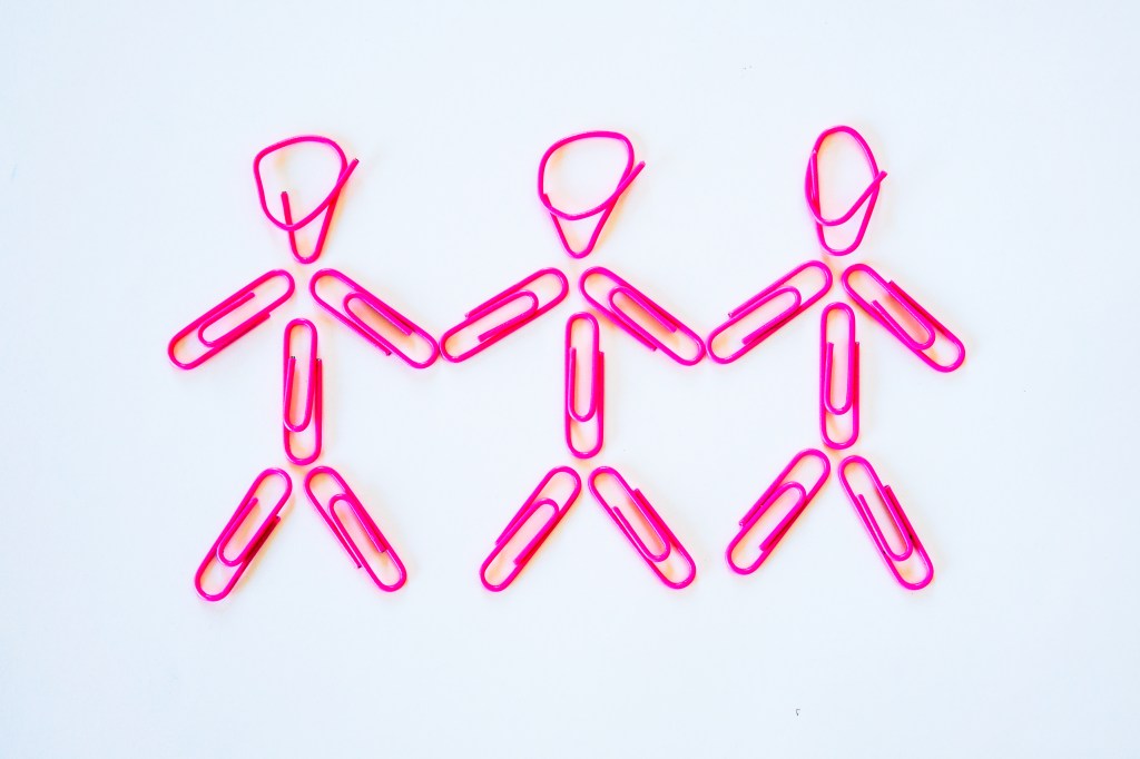 A conceptual idea of a polygamous lesbian relationship.  Three women holding hands, with arms lowered.  Represented by stereotypical pink colours for girls, it also represents happiness, alternative lifestyles and simplicity.  Studio shot on a white background.