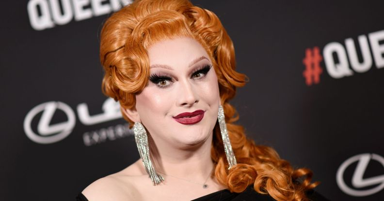 Jinkx Monsoon wearing a black dress and silver earrings on a red carpet.