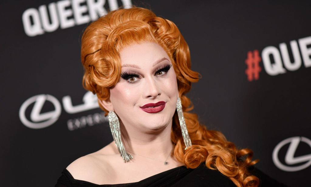 Jinkx Monsoon wearing a black dress and silver earrings on a red carpet.