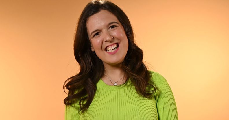 Rosie Jones smiles while wearing a neon green jumper and standing against a beige background.