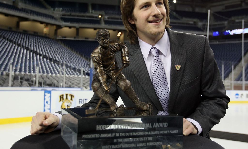 A college hockey player holding the Hobey Baker Memorial Award.