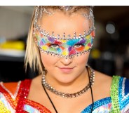 JoJo Siwa dressed in a rainbow concert outfit and rainbow makeup band across her eyes.
