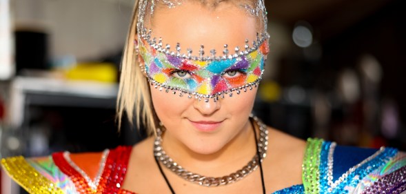 JoJo Siwa dressed in a rainbow concert outfit and rainbow makeup band across her eyes.
