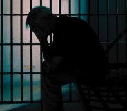 A person holding their head in their hands in a prison cell.