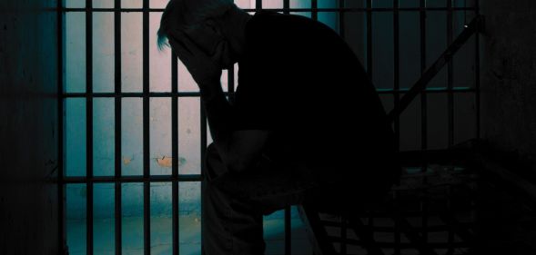 A person holding their head in their hands in a prison cell.