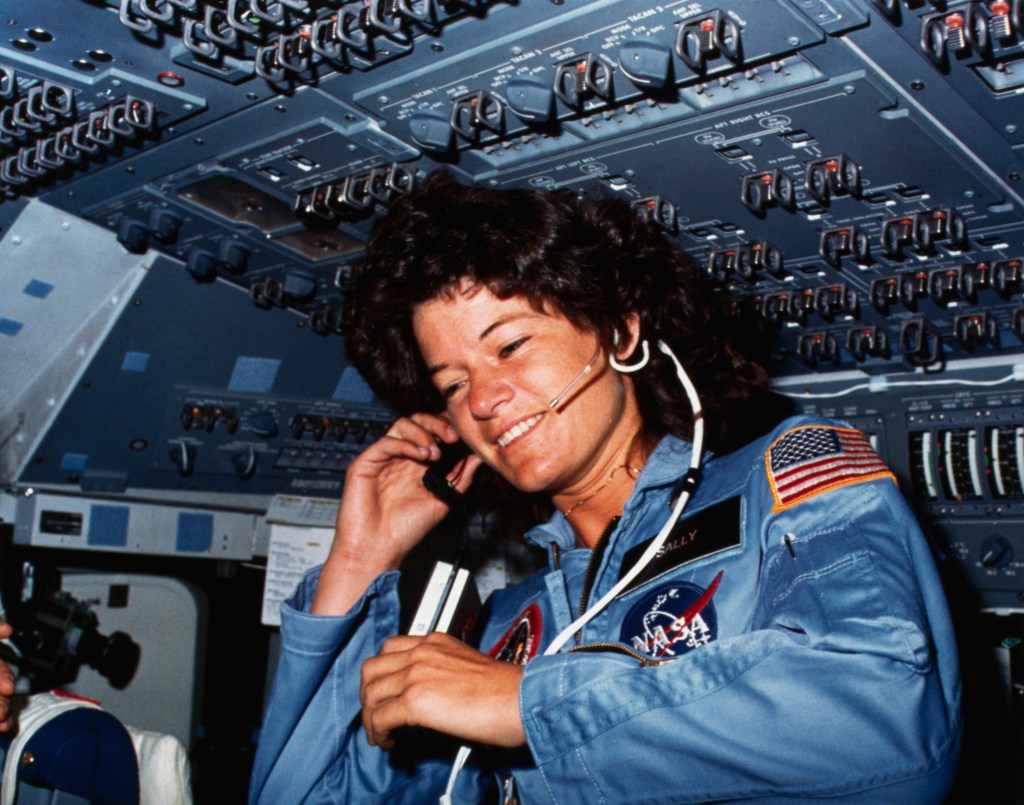 Sally Ride communicates with ground controllers from the flight deck of the Earth-orbiting Space Shuttle Challenger.