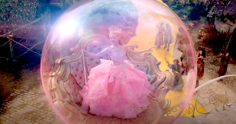 Photo shows Ariana Grande as Glinda The Good Witch floating in a pink bubble wearing a pink dress and holding a wand